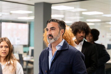 Confident male professional leading a group discussion with diverse colleagues in a coworking...