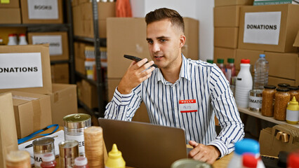 A young man uses a smartphone to send a voice message in a warehouse full of donation boxes and...