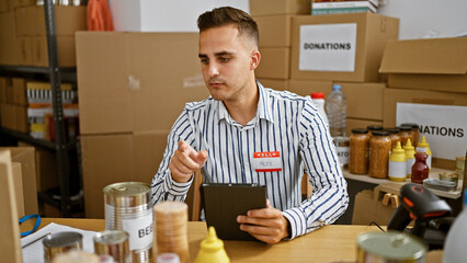 A young man in a striped shirt examines a document in a donation center filled with boxes and canned food.