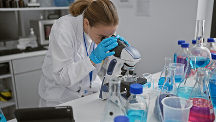 Attractive, focused blonde young woman scientist engrossed in her medical research using a microscope in lab, a portrait of determination working on scientific analysis