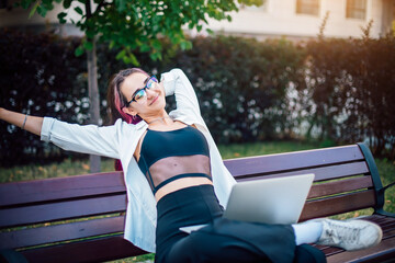 Portrait of a young woman sitting with a laptop on a bench outdoor.