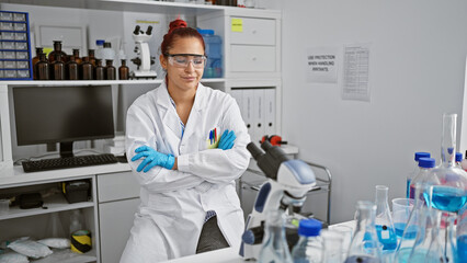 Beautiful redhead woman scientist, looking upset, sitting with crossed arms at the lab microscope. portrait of a young professional seriously involved in medical research.