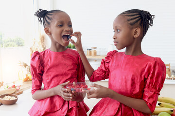 African twin girl sister with curly hair braid African hairstyle eating fresh raspberry and...