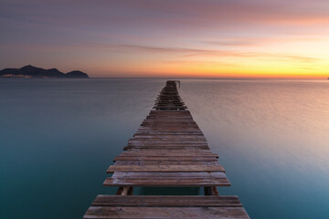 sunrise seascape with an old wooden dock leading out into the calm ocean waters