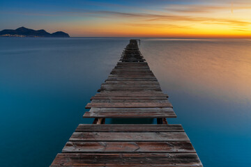 sunrise seascape with an old wooden dock leading out into the calm ocean waters of Alcudia Bay