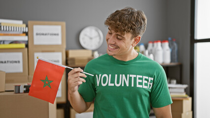 Radiant young hispanic man, proudly holding moroccan flag, contributes as smiling volunteer at...