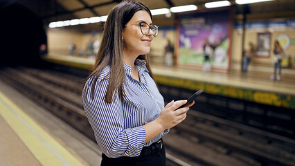 Young beautiful hispanic woman waiting for the subway using smartphone in subway station of Madrid