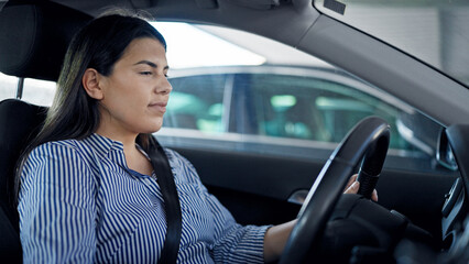 Young beautiful hispanic woman driving a car at parking lot