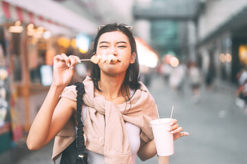 Happy asian foodie woman eating street food holding korea skewer oden