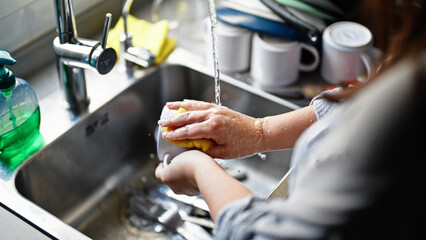 Young beautiful hispanic woman washing plates at the kitchen