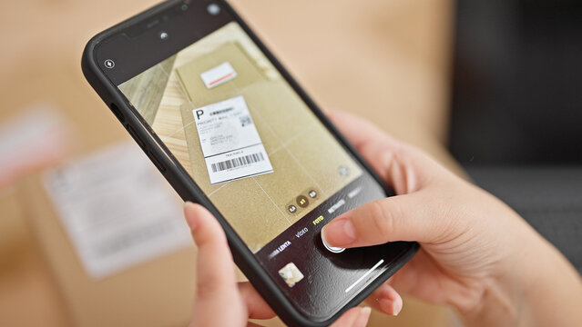 Young beautiful hispanic woman ecommerce business worker taking photo to package label at the office