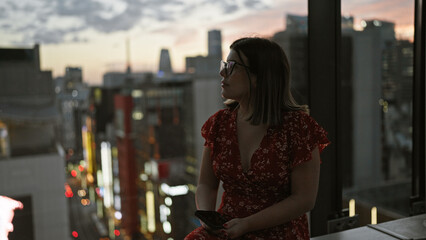 Beautiful hispanic woman glasses, looking at tokyo cityscape from sky top, using smartphone,...