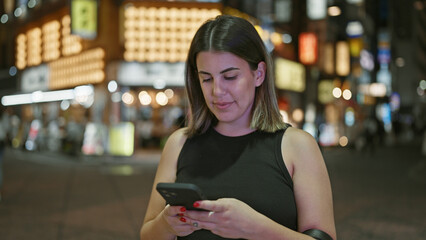 Beautiful hispanic woman engrossed in a serious phone conversation, using her smartphone on tokyo's...