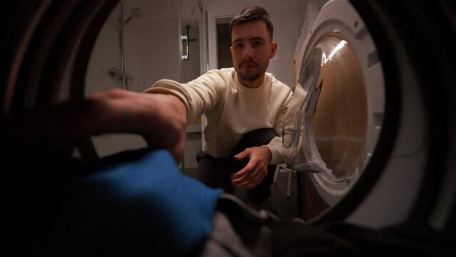 Serious man opening the washing machine and taking clean clothes at home