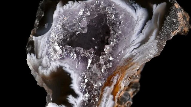 Agate - polished cross-section of geode containing quartz crystals, rotating slowly against a black background