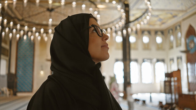 A contemplative woman wearing glasses and a hijab inside a grand mosque in doha, qatar.