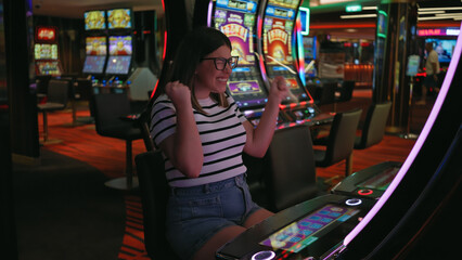 Excited young woman celebrating a win at a casino slot machine, showcasing enthusiasm and success.