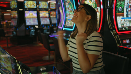 A joyful young adult woman celebrates winning at a casino slot machine.
