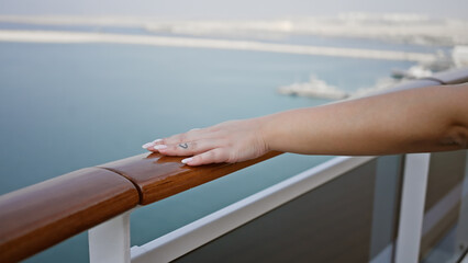 A close-up view of a woman's hand resting on the railing of a cruise ship deck with the ocean...