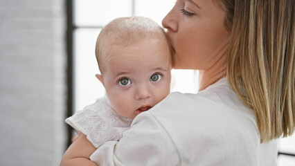 Casual and relaxed, a mother is standing, lovingly holding her baby daughter in her arms at home,...