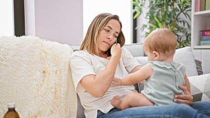 Mother talking on smartphone sitting on sofa with daughter at home