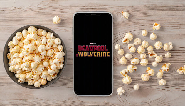 Logo of Deadpool and Wolverine movie on phone screen with popcorn on table