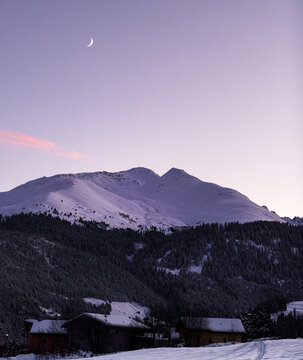 Purple sunset in Disentis, Grisons, Switzerland in the Swiss Alps. Snowy mountain and forest behind traditional village.