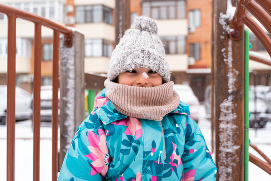 Child bundled up in a colorful jacket and woolen hat standing on a snowy playground