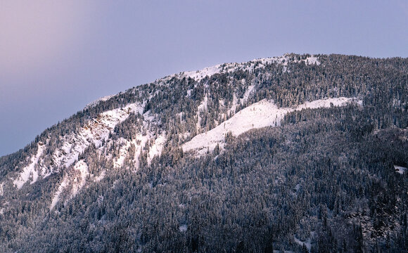 Spectacular winter sunset in Disentis, Swiss Alps. Majestic peaks, snow-covered trees, and a serene landscape bathed in pink and blue hues.