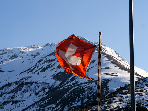 Windy Swiss Flag in front of Swiss Alps Mountain.