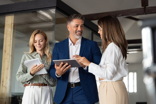 Group of diverse partners mature Latin business man and European business women discussing financial data market on tablet in office. Team of colleagues professionals business people working together.