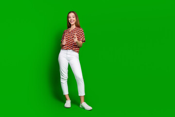 Fototapeta na wymiar Full length photo of cool friendly girl dressed print shirt white pants indicating at you isolated on vivid green color background