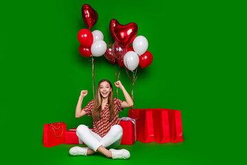 Full length photo of overjoyed teen scream yes sit near presents air balloons celebrate birthday isolated on green color background