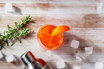 Orange cocktail and a shaker, with rosemary and ice, overhead flat lay shot on a wooden background with copy space - 739969080