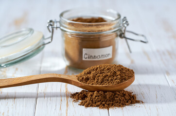 cinnamon powder poured out of a wooden spoon on a white wooden table, selective focus. - obrazy, fototapety, plakaty