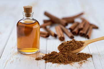 Bottle of essential cinnamon oil and cinnamon sticks on a white wooden table.