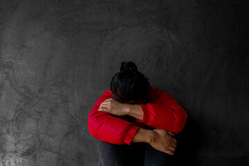 A man wearing a red  coat  sits with his head bent over and his knees hugged. A man feel very stressed.