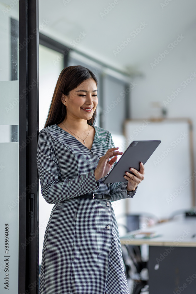 Wall mural Young asian business woman executive, female company worker or manager holding digital tablet using technology device working standing in modern corporate office.