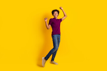 Full length photo of cheerful funky man wear trendy magenta polo raise hands fists dance festive event isolated on yellow color background