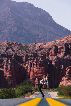 Individual playfully balancing on the road's yellow lines with the striking red formations of Los Castillos in the background