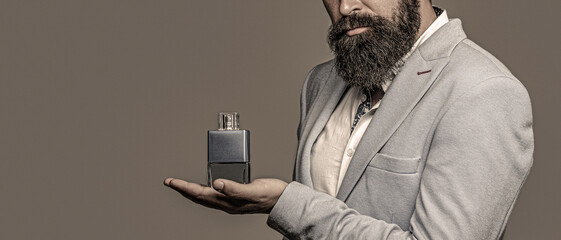 Man is holding perfume. Man holding a perfume bottle and spraying fragrance on hand. Man perfume, fragrance. Masculine perfume. Perfume or cologne bottle - obrazy, fototapety, plakaty