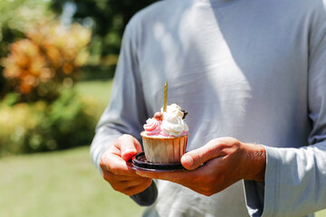 A man  holds a cupcake with a candle. Delicious Pink Birthday Cupcake