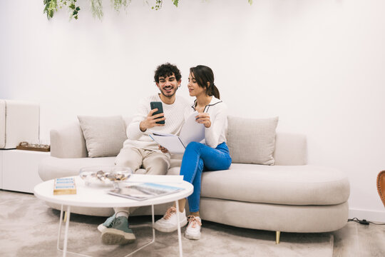 Smiling couple relaxing and using smartphone on couch