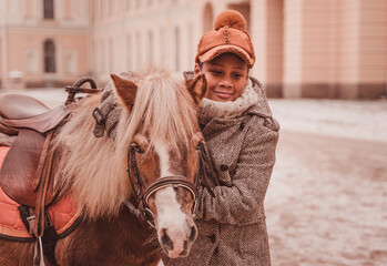 the boy stands by the pony hugging the neck and looking thoughtfully ahead