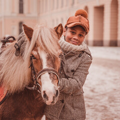 a boy stands by the pony hugging the neck and looking at the camera