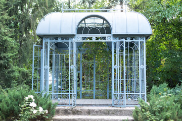 Wrought metal gazebo in summer garden. Flowers in pots near porch. Sofa in spring gazebo. Large iron blue gazebo for relax outdoor. Wedding decorations. exterior Romantic alcove. Decor autumn terrace	