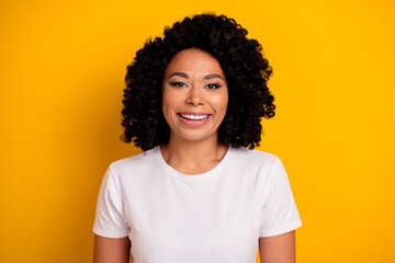 Portrait of optimistic cheerful girl with curly hairstyle wear white t-shirt toothy smiling isolated on vivid yellow color background