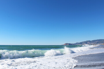 clear blue sky and waves with white foam at Mahmutlar beach in Turkey. mountains in the background