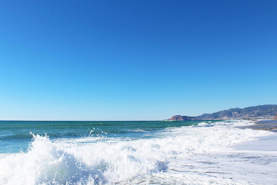 clear blue sky and waves with white foam at Mahmutlar beach in Turkey. mountains in the background