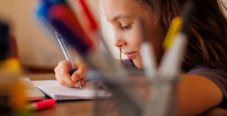 Side view of a focused little boy who is learning to write while doing his homework while sitting at his desk at home. Portrait of a smart preschooler who is learning to write. writing training. - obrazy, fototapety, plakaty